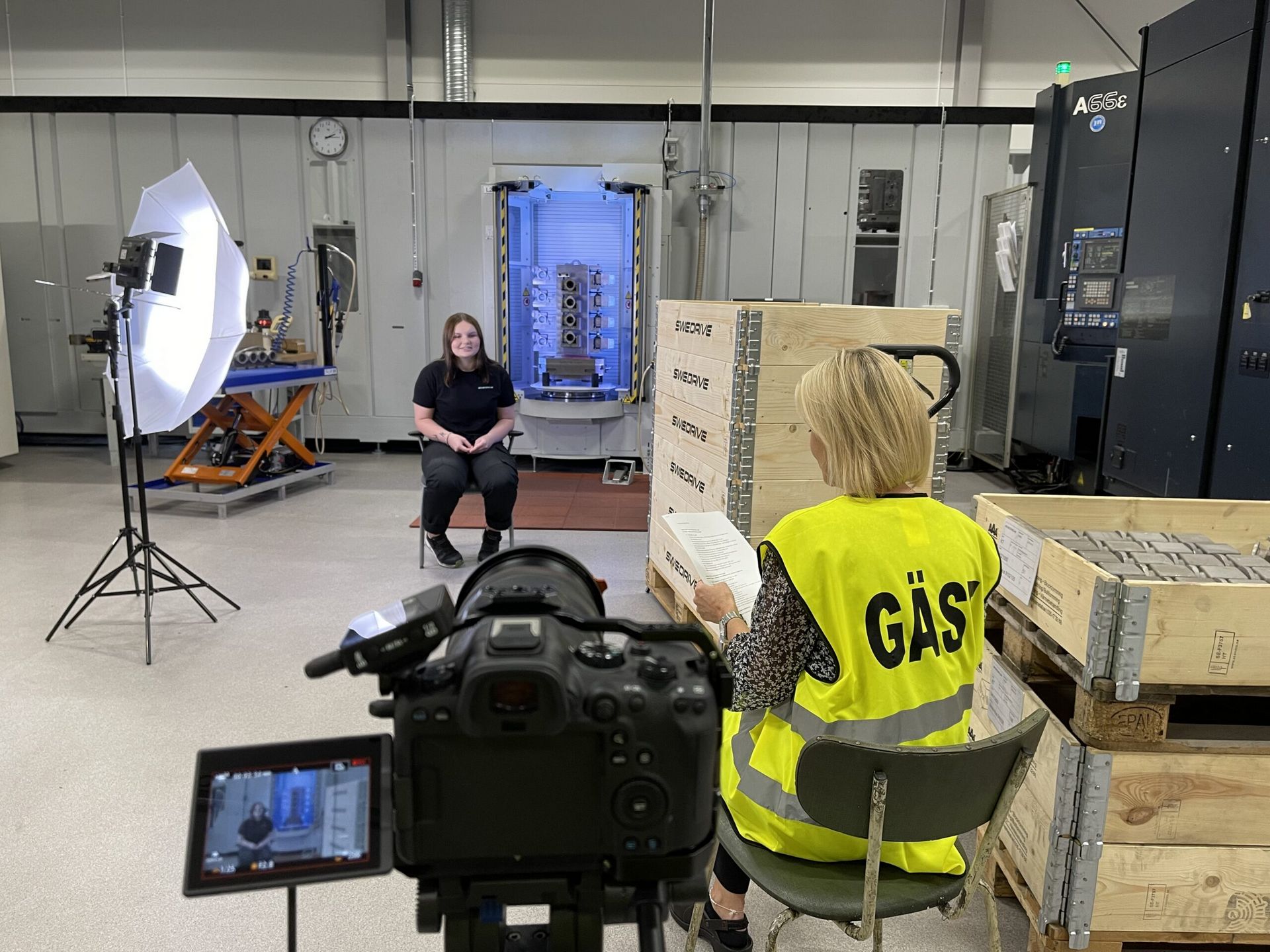 Interview with an employee in an industrial hall — interviewer with a question sheet and a camera in the foreground